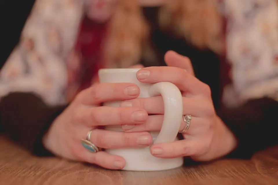 Deux mains serrées autour d'une tasse blanche posée sur une table en bois
